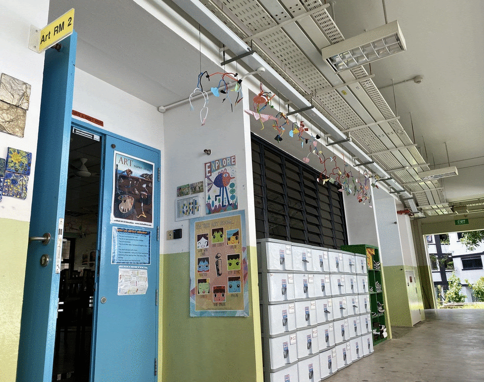 School corridor with a blue door labeled Art RM 2, colorful posters on walls, student lockers, and hanging paper decorations.